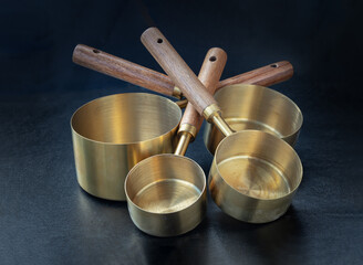 Set of Brass Measuring Cups with Wood Handles with Hanging Hole Design on dark background. Wooden &...