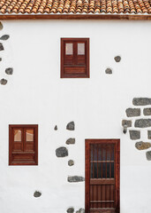 Facade of a typical two-story country house in a mountain village on Tenerife with a tiled roof, doors, unusual windows made of Canarian pine and white walls with wild stone decor, Canary Islands. - 752549390