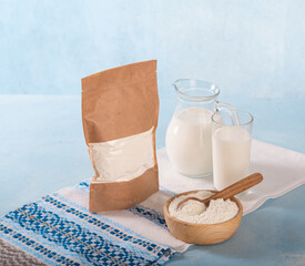 Powdered milk on a blue background and whole milk in a jug and glass