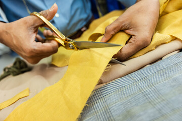 Young African American tailor cuts with scissors yellow fabric in his own atelier.