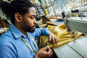 Young male African American tailor sew with a sewing machine in his own atelier