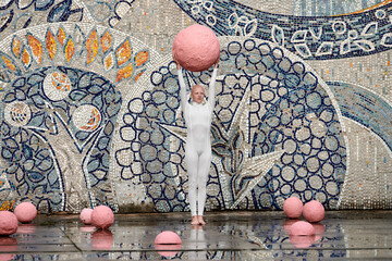 Young hairless girl with alopecia in white futuristic suit dancing outdoor smoothly holding pink ball on abstract mosaic Soviet background, symbolizes self expression and cultural identity