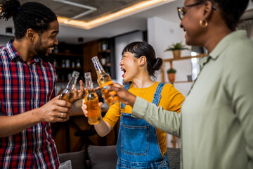 Multiethnic group of friends at home dancing and singing with beer in their hands.