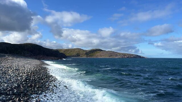 Beach in Teriberka, dragon eggs. Mountains surround the bay, and waves roll onto the beach with dragon eggs. Rounded stones lying on the shore of the North Sea.Kola Peninsula,Murmansk region,Russia 4К