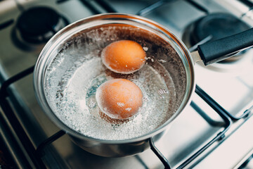 Saucepan stainless steel with two boiling eggs breakfast in a water on a gas stove top view. - 752556318