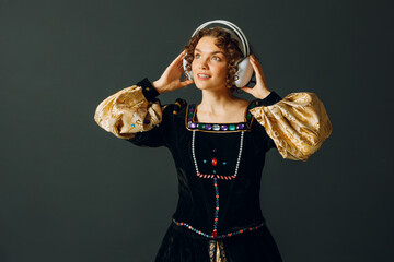 Portrait of a young aristocratic woman with headphones on her head and dressed in a medieval dress listens classical music - 752557395