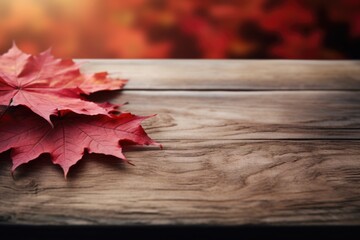 Naklejka na ściany i meble A couple of red leaves resting on a wooden table. Ideal for autumn-themed designs