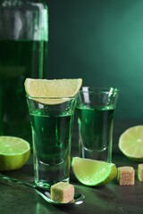 Absinthe in shot glasses, spoon, brown sugar cubes and lime on gray textured table, closeup....