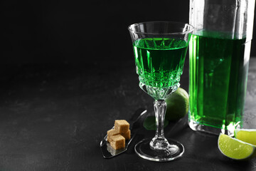 Absinthe, spoon, brown sugar and lime on black table, space for text. Alcoholic drink