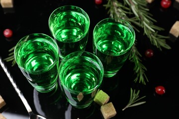 Absinthe in shot glasses, cranberries, rosemary and brown sugar on mirror table, closeup. Alcoholic drink