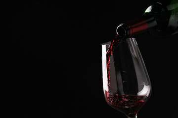 Pouring tasty red wine from bottle into glass on black background, closeup. Space for text
