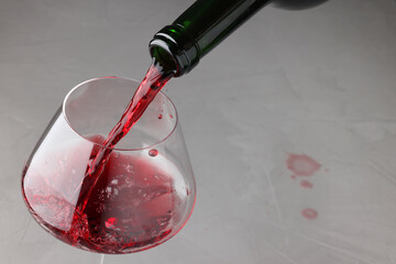 Pouring tasty red wine in glass at gray table, closeup. Space for text