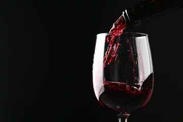 Behang Pouring red wine into glass against black background, closeup. Space for text © New Africa