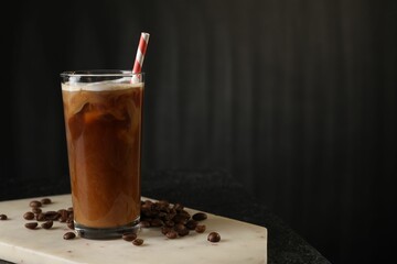 Refreshing iced coffee with milk in glass and beans on table against dark gray background, space for text