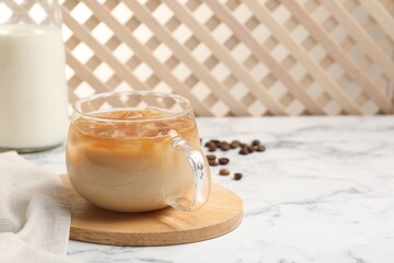 Refreshing iced coffee with milk in glass cup on white marble table, space for text