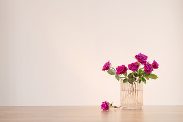 purple roses in glass vase on wooden table 