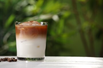 Glass of iced coffee and beans on white wooden table outdoors. Space for text