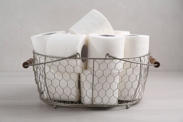 Soft toilet paper rolls in metal basket on white wooden table, closeup