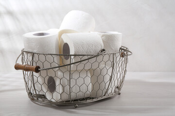Soft toilet paper rolls in metal basket on white wooden table, closeup