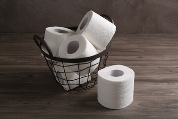 Soft toilet paper rolls in metal basket on wooden table