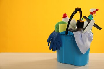 Different cleaning products in bucket on wooden table against yellow background, space for text