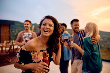 Cheerful woman having fun on summer party with friends on terrace at sunset.