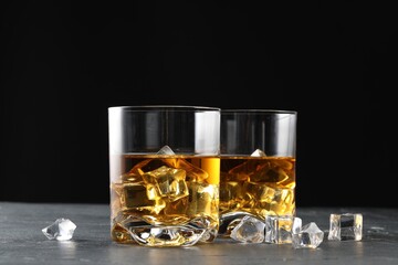 Whiskey and ice cubes in glasses on black table, closeup