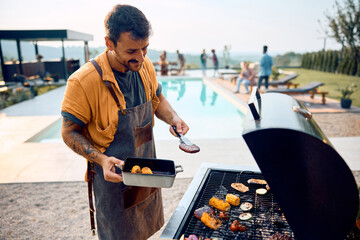 Young happy man preparing barbecue by pool.