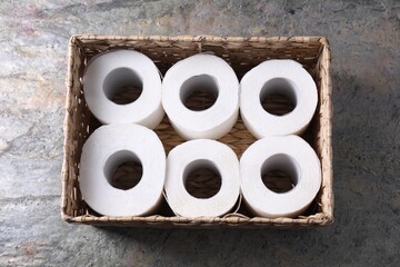 Toilet paper rolls in wicker basket on textured table, top view