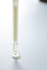 Dripping moisturizing serum from pipette on light grey background, closeup