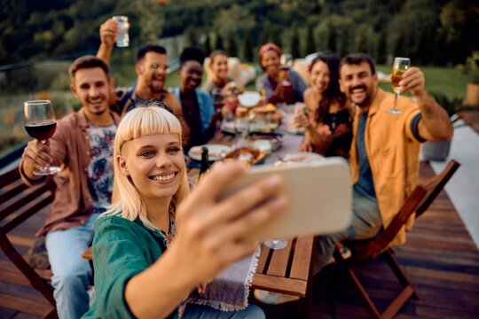 Happy woman taking selfie with friends while gathering for lunch party on patio.