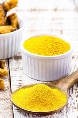 turmeric powder, saffron roots in wooden bowl on white table