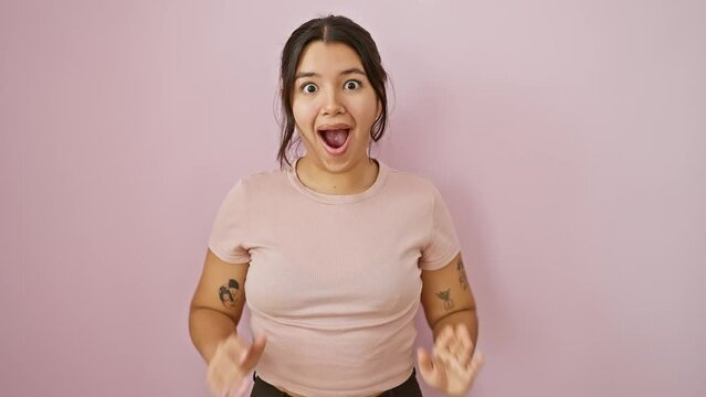 Shocked and amazed, beautiful young hispanic woman standing over isolated pink background. with a surprised expression, she exhibits a mix of fear and excitement written all over her face