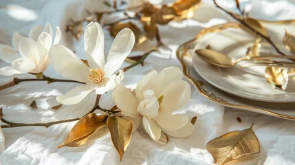 Gordijnen A branch with beautiful white magnolia flowers lies on a white tablecloth next to gold leaves and dishes. Nature background. Springtime © vannet