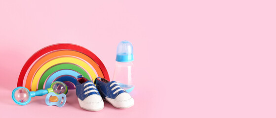 Stylish baby shoes with pacifier, rattle and bottle of milk on pink background