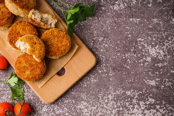 Wooden board of tasty meat cutlets on grey background