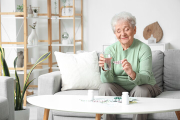 Senior woman with glass of water and pills at home - obrazy, fototapety, plakaty