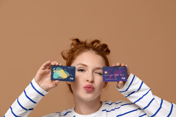 Beautiful young woman with credit cards blowing kiss on brown background