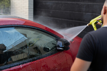 Man pressure washing a red car's window