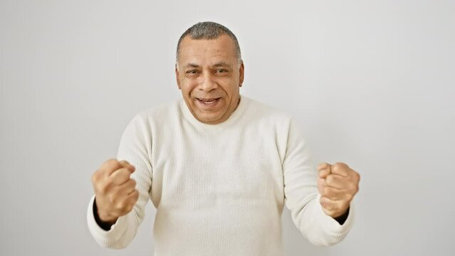 Ecstatic middle age latin man, wearing a sweater, exuding triumph as he proudly raises his arms in excitement, standing isolated on a white background, screaming in celebration of his victory