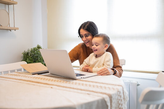 A heartwarming moment as a smiling mother embraces her son while they both engage with content on a laptop at home