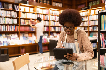 Young African American woman using tablet in a bookstore setting