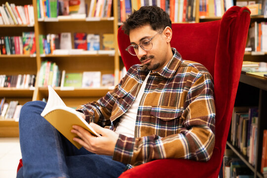 Man in glasses reading a book in a cozy library corner