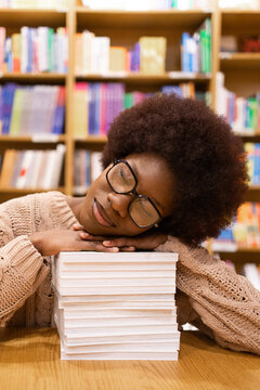 Relaxed young African American woman resting head on stack of books