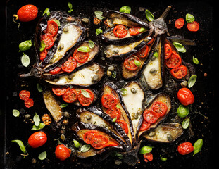 Baked eggplants in the fan shape stuffed with cherry tomatoes and mozzarella cheese on a black background, top view