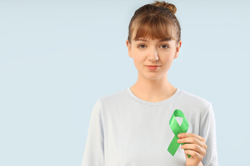 Young woman with green ribbon on light background. Glaucoma awareness month