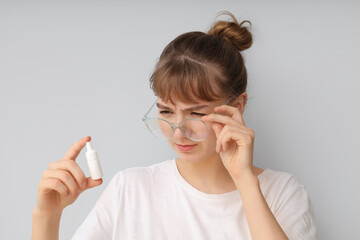 Young woman in eyeglasses with drops squinting on light background, closeup. Glaucoma awareness...