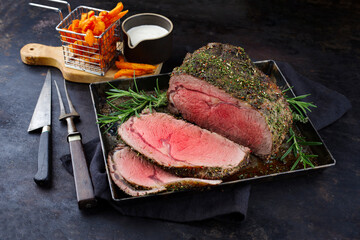 Traditional Commonwealth Sunday roast beef sliced with herbs and French fries served as close-up on...