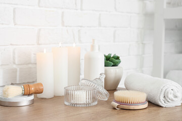 Fototapeta na wymiar Candles and bath supplies near brick wall in bathroom