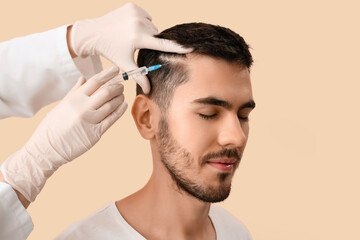 Young man receiving injection for hair growth on beige background, closeup